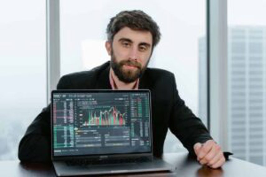 A man sits at a desk and shows data on his laptop