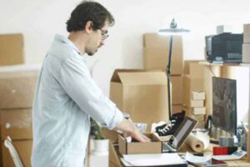 A man packing boxes of products in front of his computer