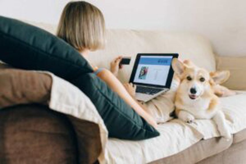 A woman shops online with her dog next to her