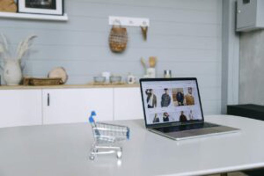 A laptop showing an online store next to a mini shopping trolley