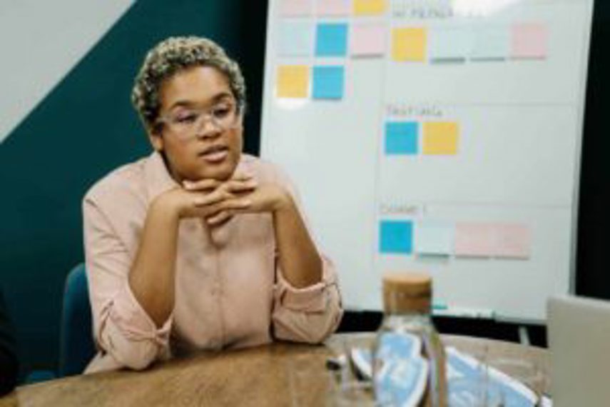 A woman thinking at a desk with a chart behind her