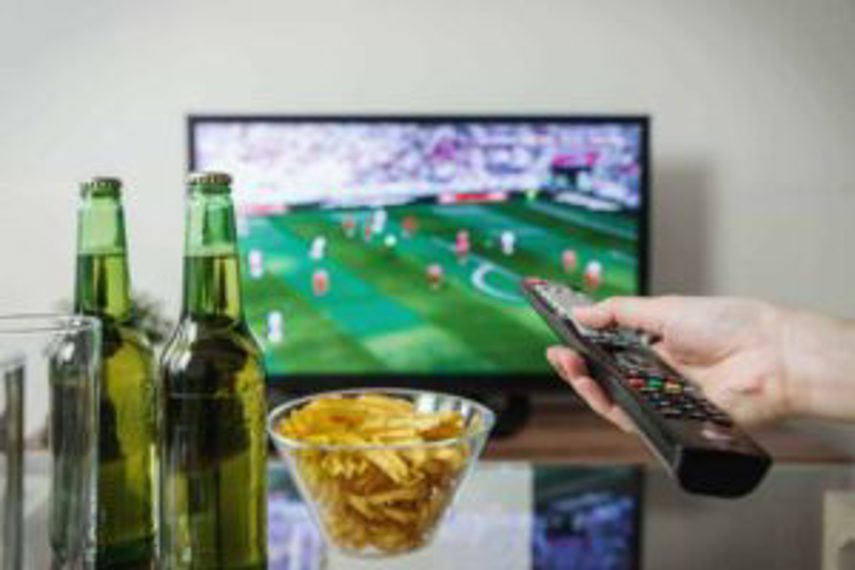 A person watches football on TV with chips and beer