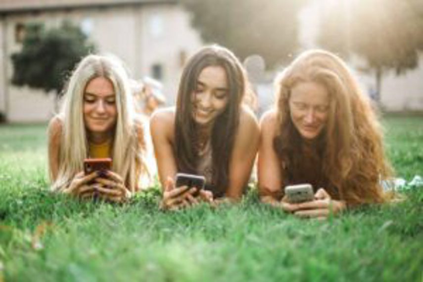 Three women looking at social media while lying on the grass