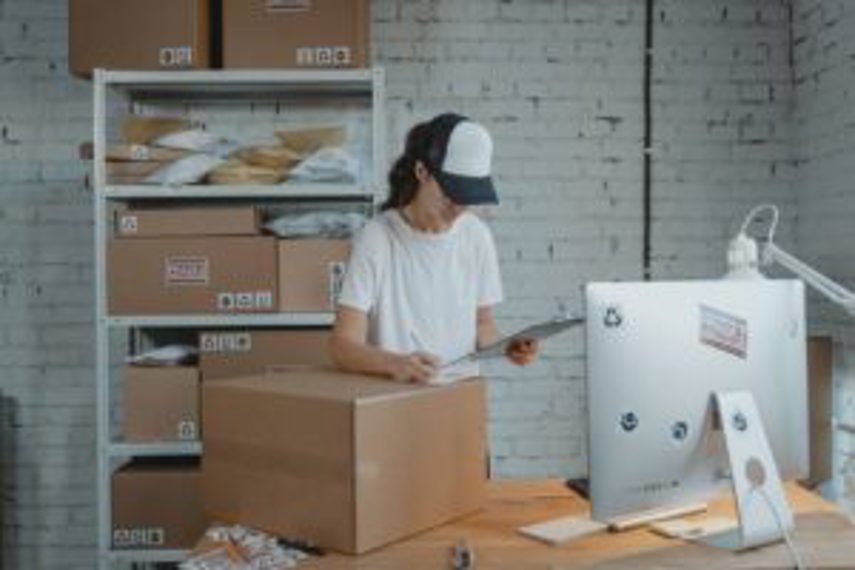 A woman in a warehouse checks packages on a clipboard