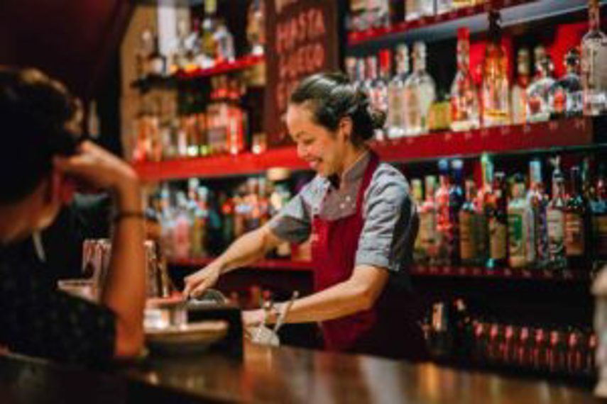 A woman serves drinks at a stocked bar