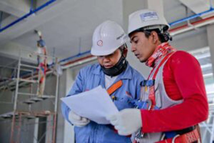 Two men wearing hard hats look at plans