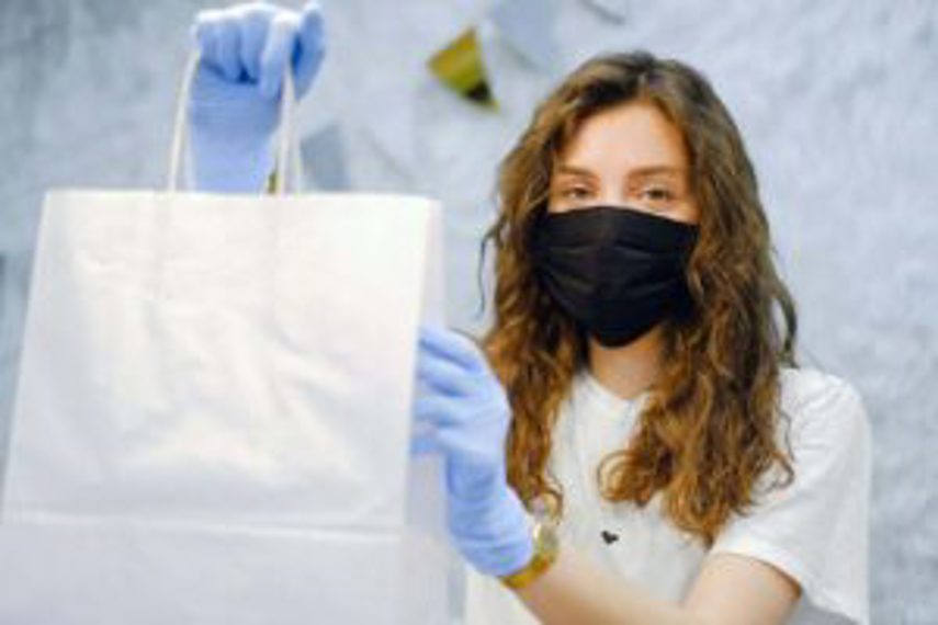 A masked woman hands over a shopping bag