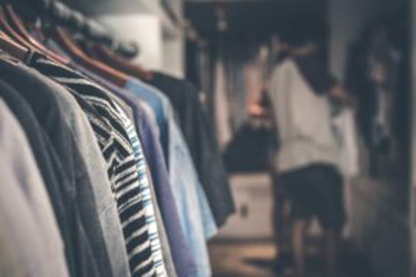 Clothing hangs on a rack in the foreground while customers browse in the background