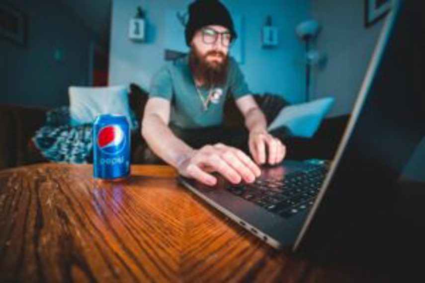 A man works on his computer with a can of Pepsi beside him