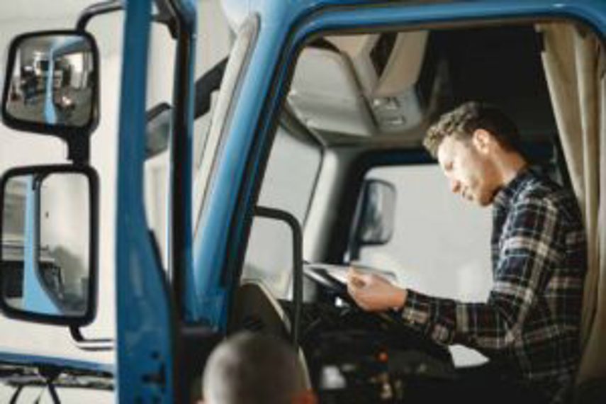 A man sits in the cab of his truck reading a document