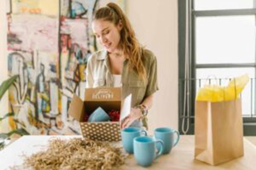 A woman holds up a package with coffee cups in it