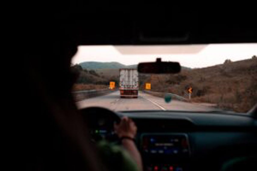 A person drives with a truck seen through the windscreen